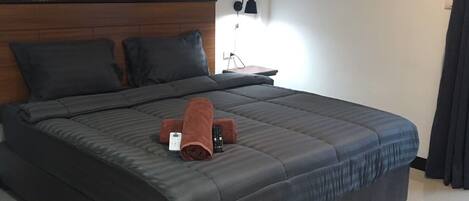 A modern hotel room with a large bed, a nightstand, a lamp, and an air conditioning unit.