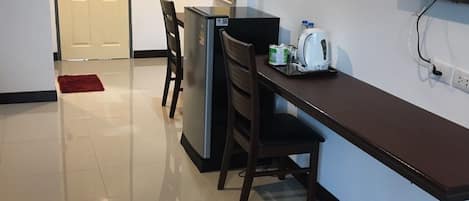 A modern kitchen with a refrigerator, a microwave, and a toaster on the counter. There is a dining table with chairs and a red rug on the floor. A TV is mounted on the wall.