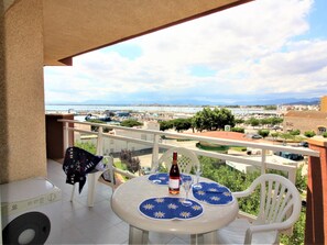 A balcony with a table set for two, a bottle of wine, and a view of a marina and cityscape.