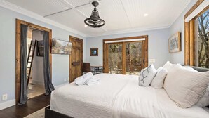 Ein Schlafzimmer mit einem großen Bett, einem Deckenventilator, Holztüren und Blick ins Freie.