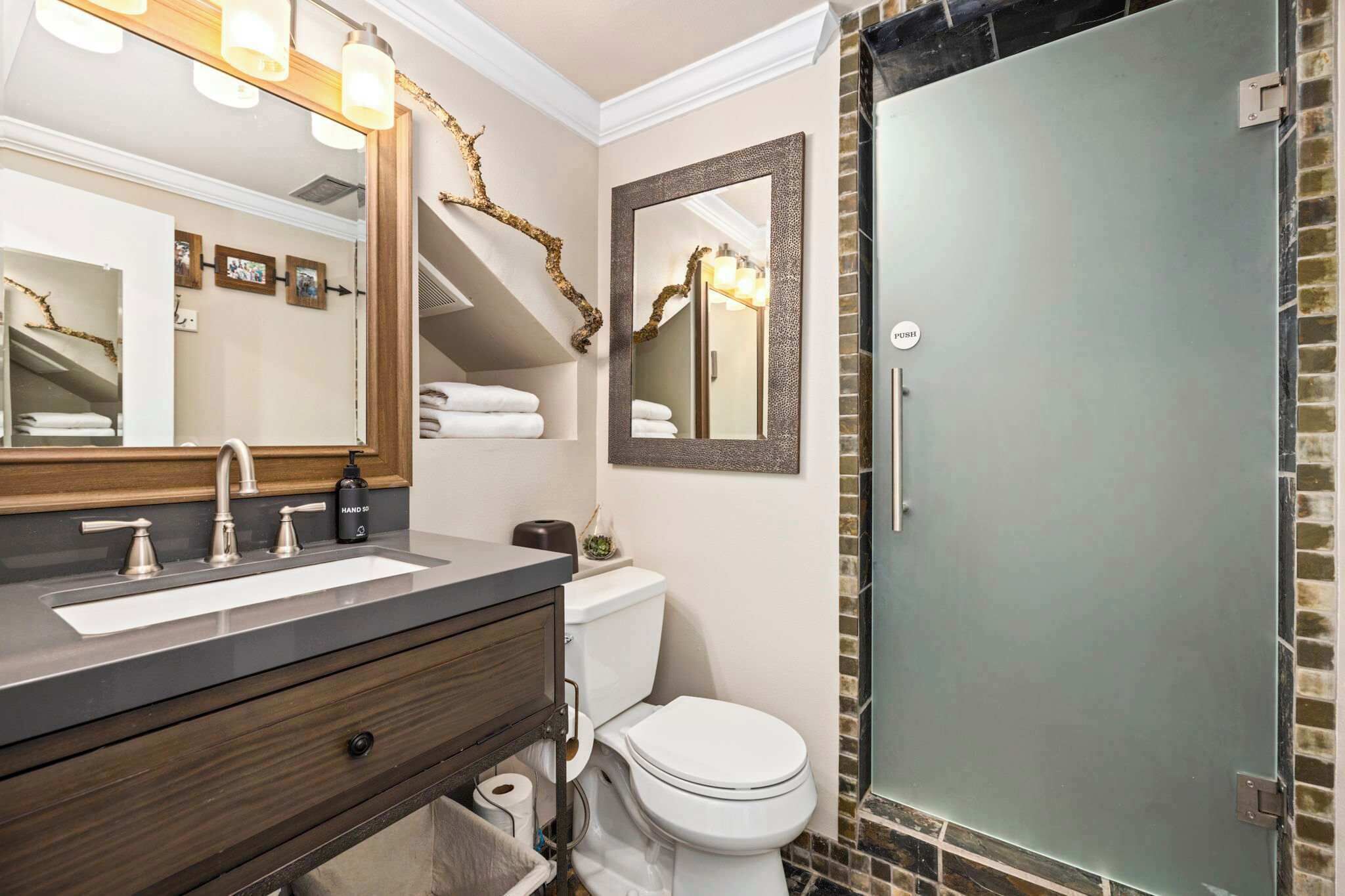 Un bagno con uno specchio grande, un lavabo con piano d'appoggio scuro, un water e un box doccia in vetro.