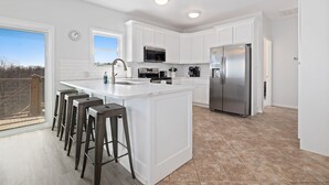Una cocina moderna con muebles blancos, un refrigerador de acero inoxidable y una isla grande con taburetes de bar.