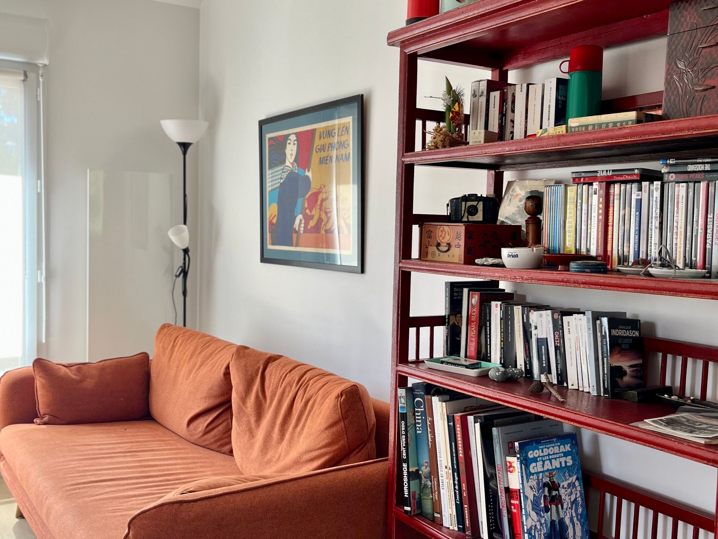 Ein Zimmer mit einem roten Bücherregal voller Bücher, einem braunen Sofa und einem gerahmten Bild an der Wand.