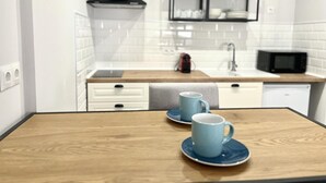 A modern kitchen with white cabinets, a black range hood, and a microwave. There are two blue cups on a wooden table. - Modern, functional studio 15 min from center with Wi-Fi and air conditioning (Málaga)