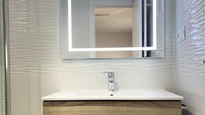 A bathroom with a white sink, a wooden vanity, and a mirror with a light strip. - Modern, functional studio 15 min from center with Wi-Fi and air conditioning (Málaga)