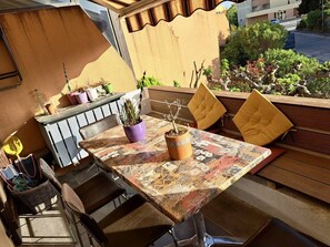 An outdoor patio with a table and chairs, potted plants, and a view of the street.