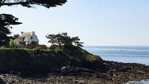 Une maison située sur la côte, avec un rivage rocheux, une colline herbeuse et une vue dégagée sur la mer.