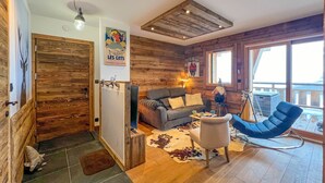 Een gezellige woonkamer met een houten plafond, een bank, een blauwe stoel en een rustieke deur.