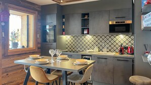 Een moderne keuken met een eethoek, met een houten plafond, grijze kastjes, een decoratieve spatwand en een ingebouwde oven.