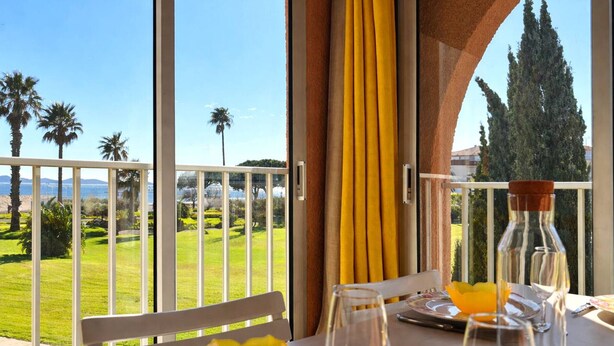 A dining table with a view of a golf course and a body of water.