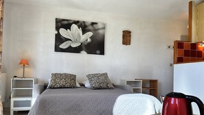 A bedroom with a bed, pillows, a bedside table with a lamp, a coffee maker, and a framed picture on the wall.