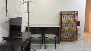 Habitación con una televisión en un mueble, una mesa con sillas, un estante decorativo y un ventilador de techo.