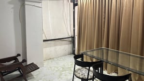 Una habitación con una mesa y sillas de vidrio, un banco de madera, cortinas color beige y suelo de baldosas.