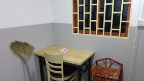 Una habitación pequeña con una mesa y silla de madera, un escoba y una cesta de mimbre.