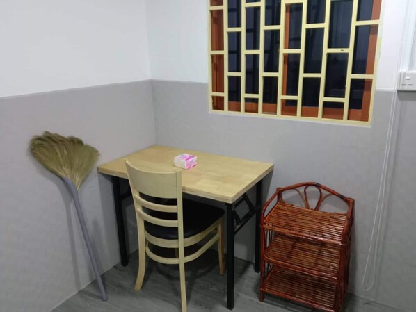 A small room with a wooden table and chair, a broom, and a wicker basket.