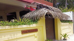 Un bâtiment jaune avec une entrée surmontée d’un toit de chaume, une enseigne indiquant « Sea Breeze », et de petites plantes en pot disposées à l’entrée.