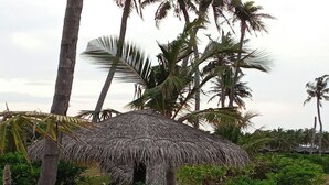 Une plage avec un parasol en chaume, une chaise longue bleue et des palmiers.
