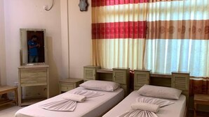 Une chambre d’hôtel avec deux lits simples, un ventilateur de plafond, un appareil de climatisation, un bureau avec une chaise et une fenêtre avec des rideaux à rayures.