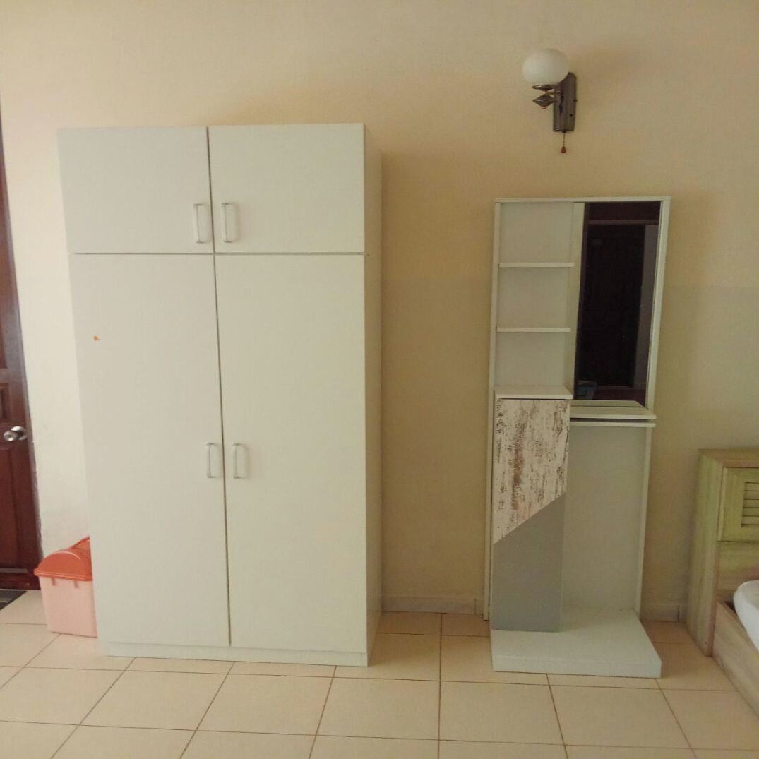 Een kamer met een grote witte garderobe, een klein wandrek en een bed met een houten hoofdbord.
