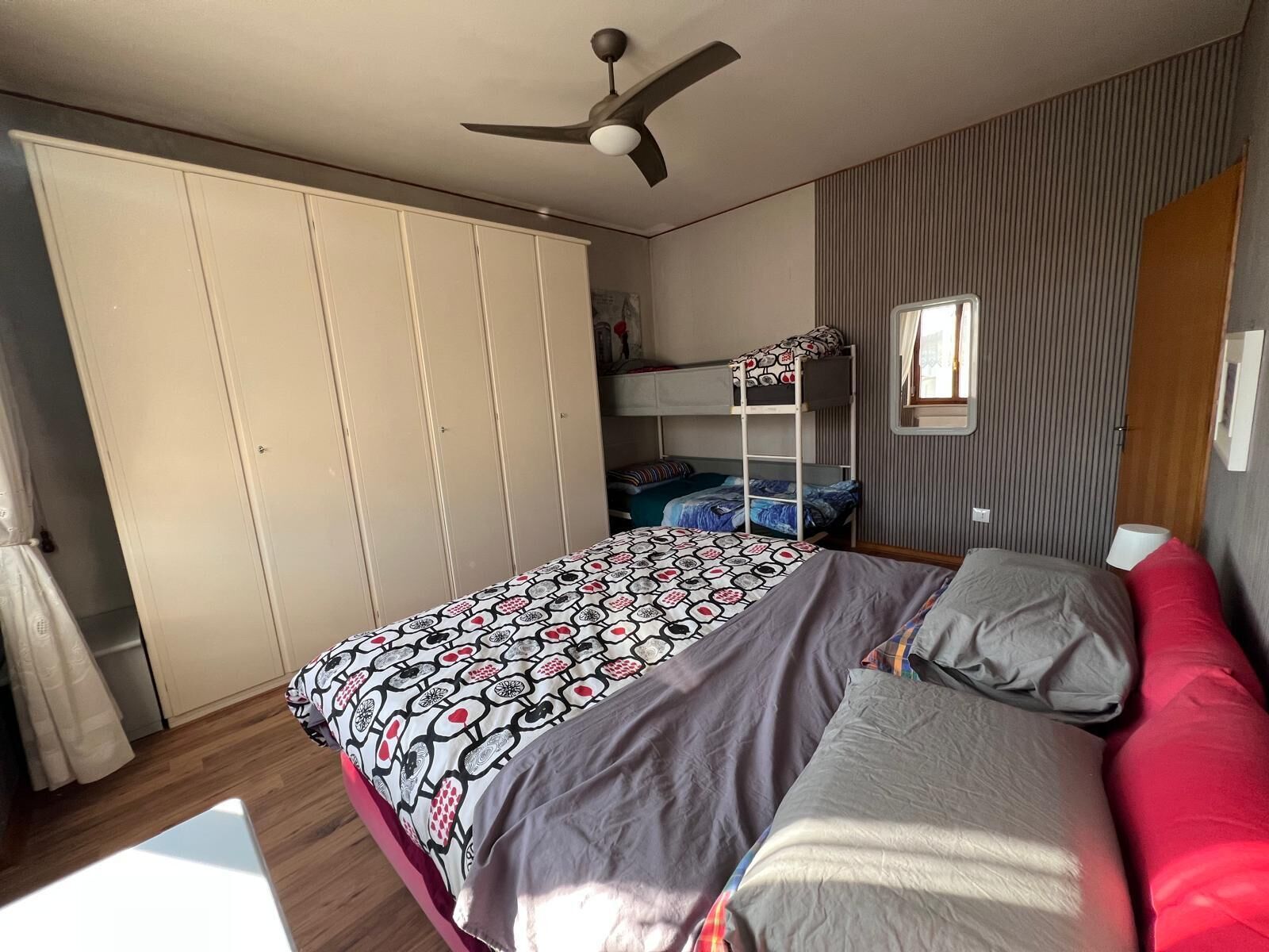 A bedroom with a bunk bed, a wardrobe, a ceiling fan, and a window with blinds.
