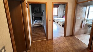 Un pasillo con una litera, un baño con lavamanos y una ducha.