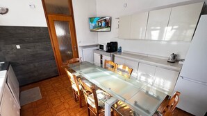 Una cocina moderna con una mesa de comedor de vidrio, sillas de madera, armarios blancos y un televisor en la pared.