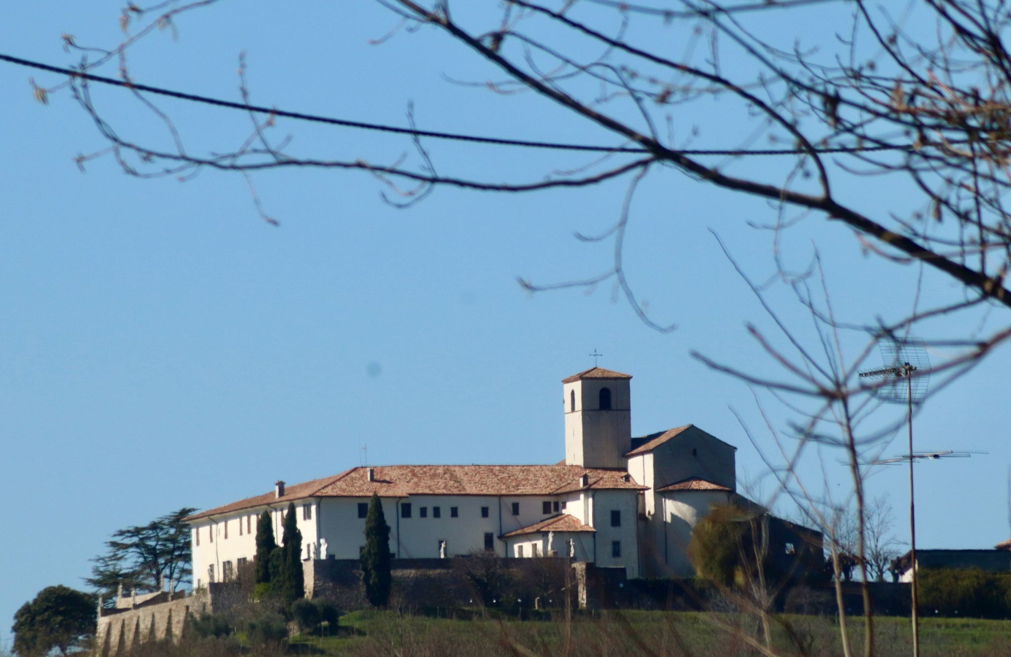 A large, historic building with a prominent bell tower, surrounded by trees and open fields.
