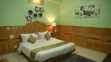 Un dormitorio con cabecera de madera, cama con ropa de cama blanca y detalles verdes, una lámpara de pared y una obra de arte floral.