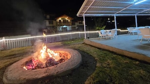 A covered outdoor seating area with a fire pit in the foreground. - Jibhi Village (Banjar)