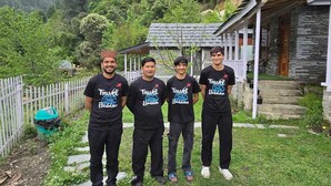 Four individuals standing in a grassy area with a stone building in the background. - Jibhi Village (Banjar)