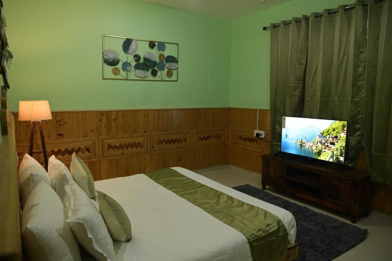 A room with a bed, a television, a wall art piece, and wooden paneling.