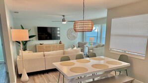 A modern living room with a sofa, a dining table with placemats, a ceiling fan, and a TV. - New Listing Discount! Coconut Cove - Heated, Saltwater Pool/Spa - fully renovated! (Naples)