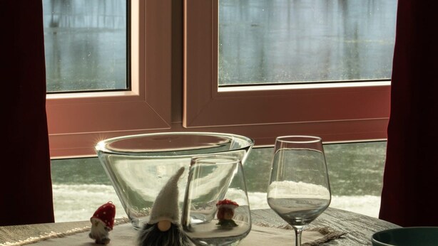 A dining table with a glass bowl, wine glass, and plates, set against a window with a view of a snowy landscape. - Lakefront Family Retreat (Harzgerode)