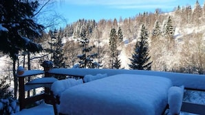 A snow-covered wooden deck with a bench and a table, overlooking a forested area. - Lakefront Family Retreat (Harzgerode)