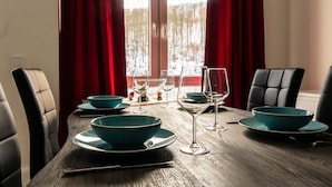 A dining table set with teal bowls and wine glasses, red curtains, and a view of a snowy landscape through a window. - Lakefront Family Retreat (Harzgerode)