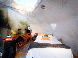 Ein gemütliches Schlafzimmer im Dachgeschoss mit einem großen Bett, einem hölzernen Schreibtisch, einem Kamin und einem Wandgemälde.