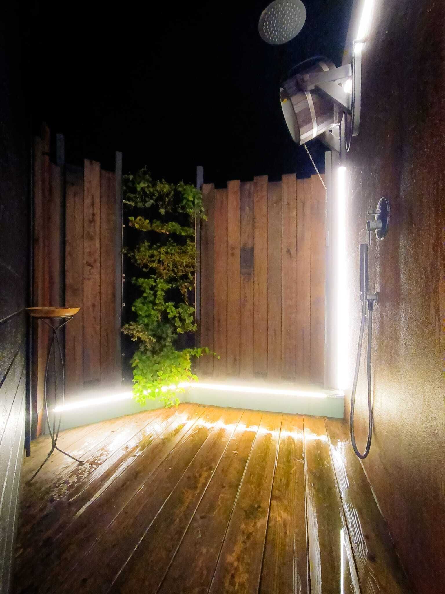 Una terraza de madera con ducha integrada y un pequeño espacio para sentarse.