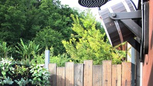 Een houten hek met een metalen poort, omgeven door weelderige begroeiing en een houten terras.