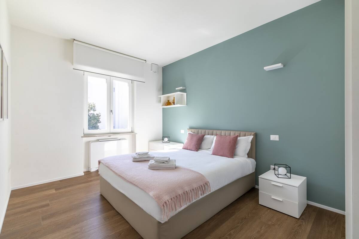 A bedroom with a bed, bedside tables, a window, and a wall-mounted shelf.