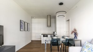 A modern living room with a sofa, a coffee table, and a TV. There is a dining area with a table and chairs, and a kitchen in the background. - Le Barche66 Venice Apartments (Mestre)