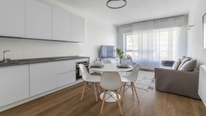 A modern kitchen with white cabinets, a dining area with a round table and chairs, and a grey sofa in a bright living space with large windows. - Le Barche66 Venice Apartments (Mestre)