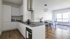 A modern kitchen with white cabinetry, a central island, and a dining area with a table and chairs. - Le Barche66 Venice Apartments (Mestre)