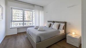 A modern bedroom with a large window, a bed with neatly folded towels, a bedside table with a lamp, and a nightstand. - Le Barche66 Venice Apartments (Mestre)