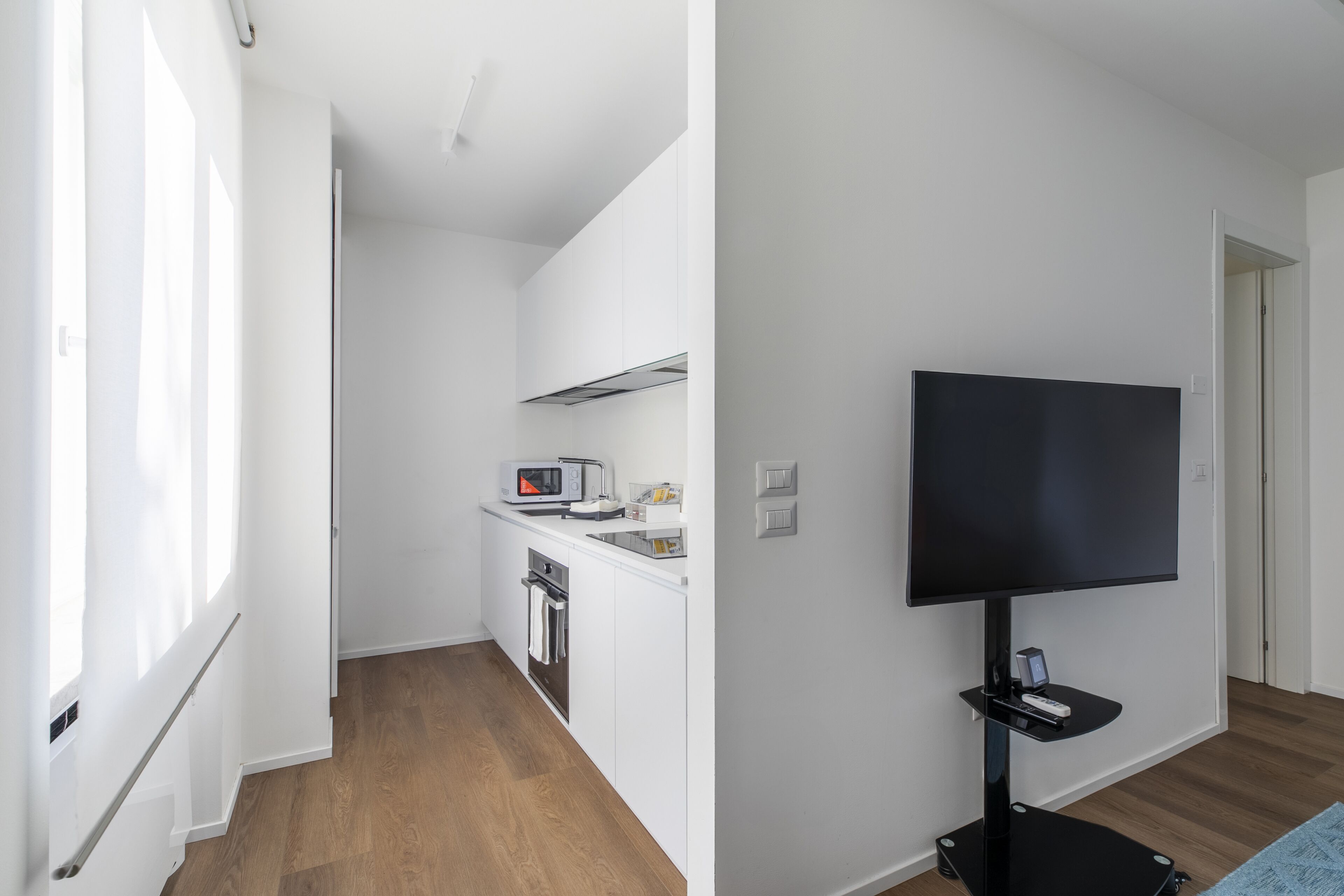 Una cocina moderna con armarios blancos, un microondas y un tostador. Un televisor de pantalla plana está montado en la pared.