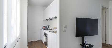 Una cocina moderna con armarios blancos, un microondas y un tostador. Un televisor de pantalla plana está montado en la pared.