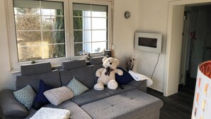 A grey sofa with multiple cushions, a white fluffy throw, and a teddy bear. - Super nice and completely renovated vacation home between Szczecin Lagoon and Usedom (Ducherow)