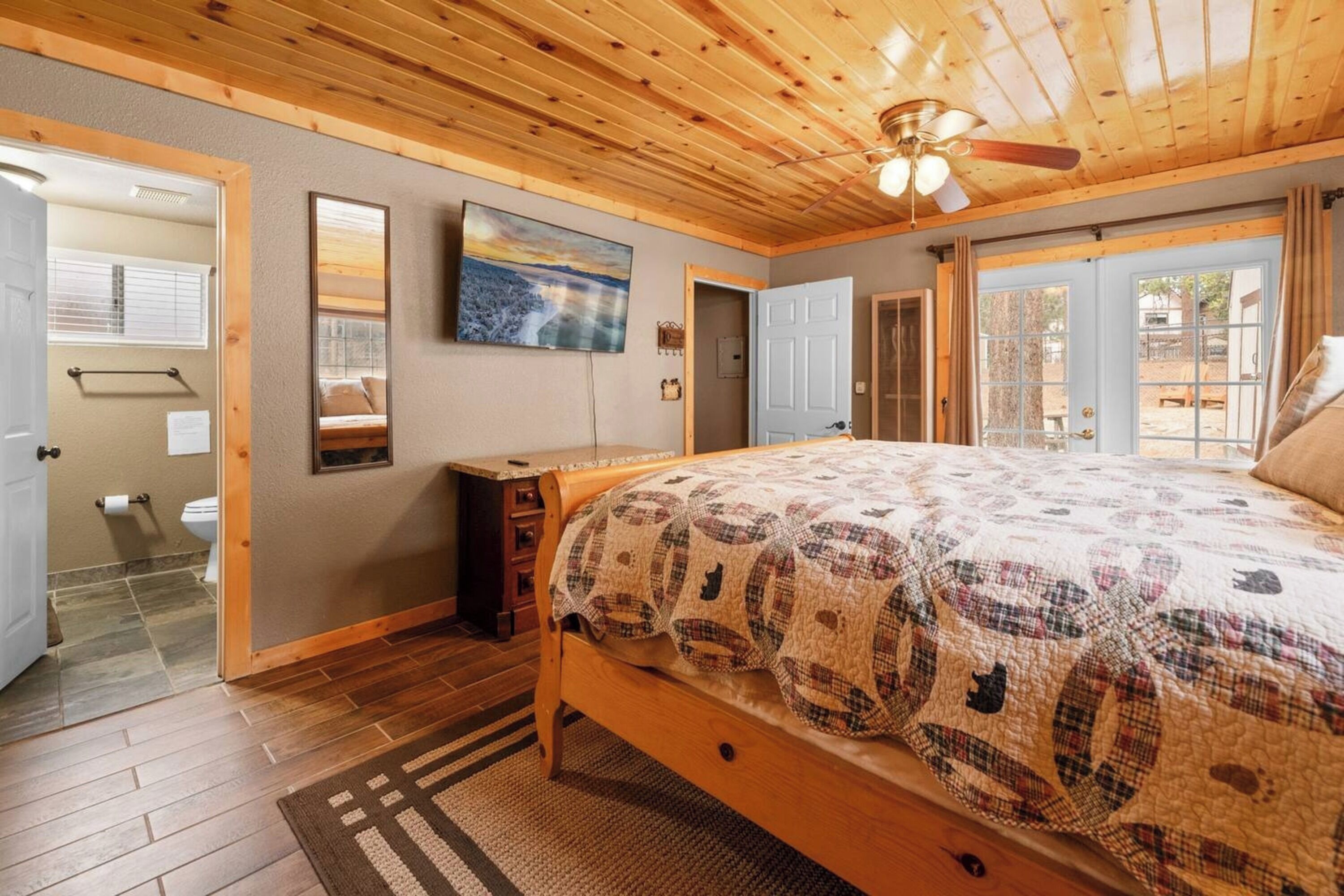 Un dormitorio con techo de madera, una cama con manta estampada, un cuadro en la pared y vistas a través de la puerta.