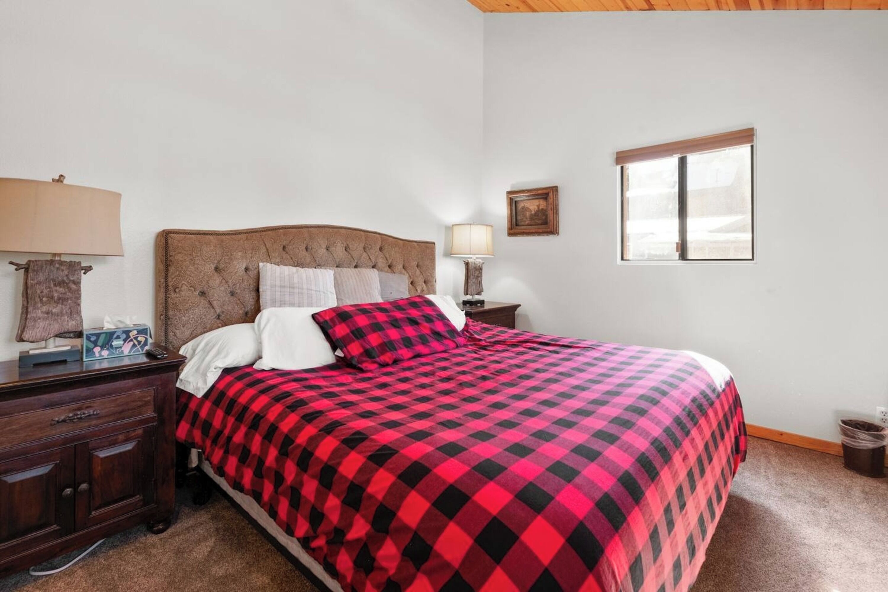 A bedroom with a large bed, a nightstand with a lamp, a dresser, and a window.