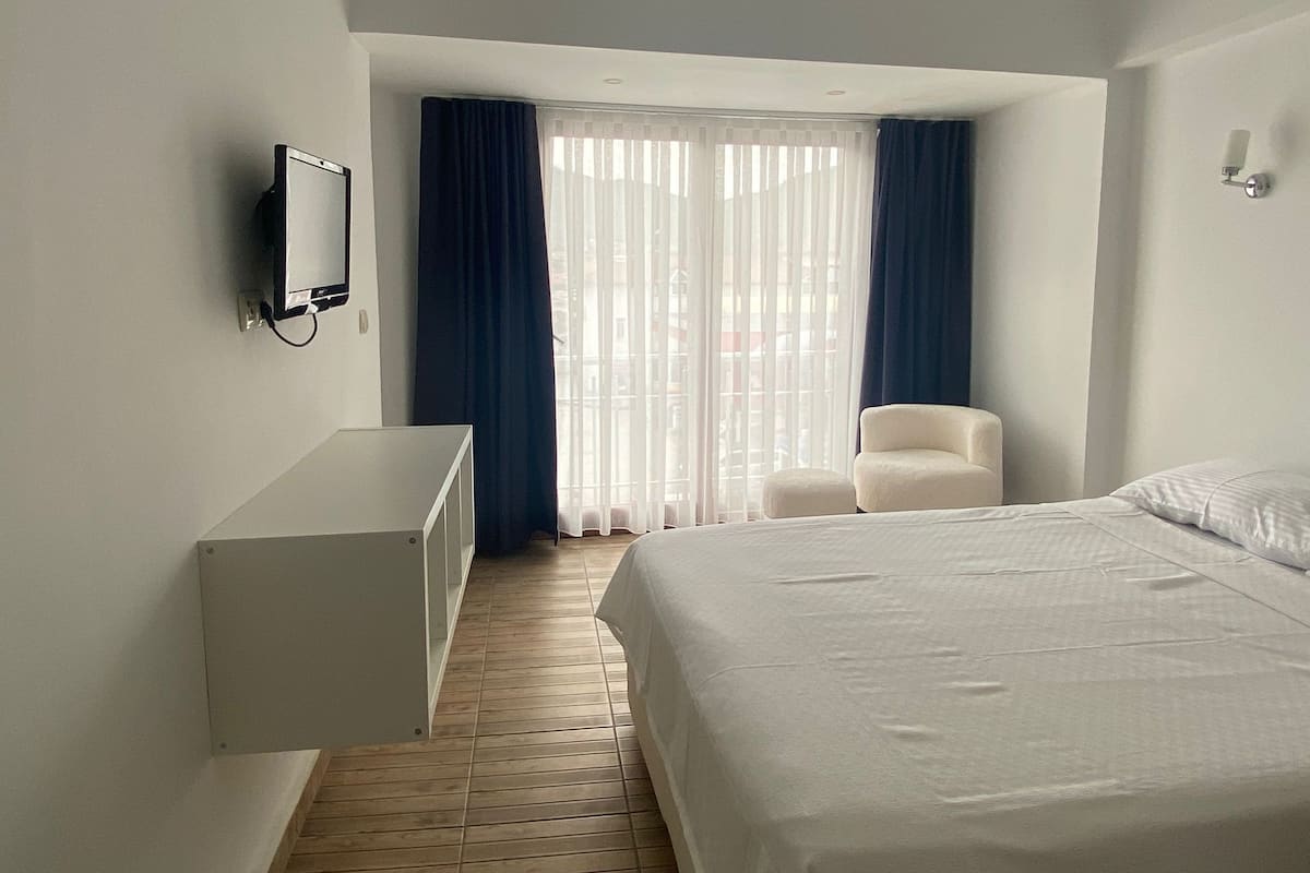 Une chambre d’hôtel avec un lit, une chaise, un bureau et une fenêtre avec des rideaux.