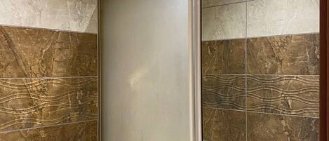 A bathroom with a toilet, a shower enclosure, and marble-patterned walls.